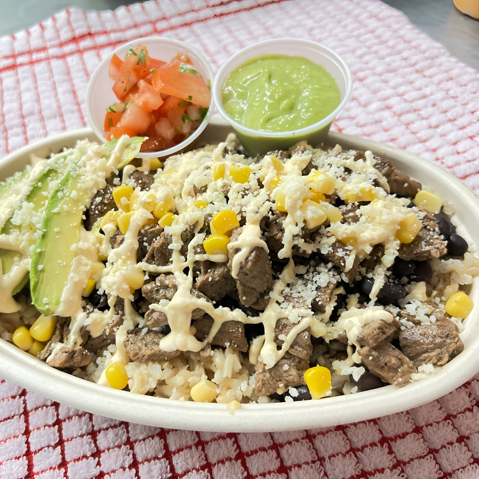 A Latin Kitchen steak bowl with rice, corn, avocado, cheese, and two side sauces.